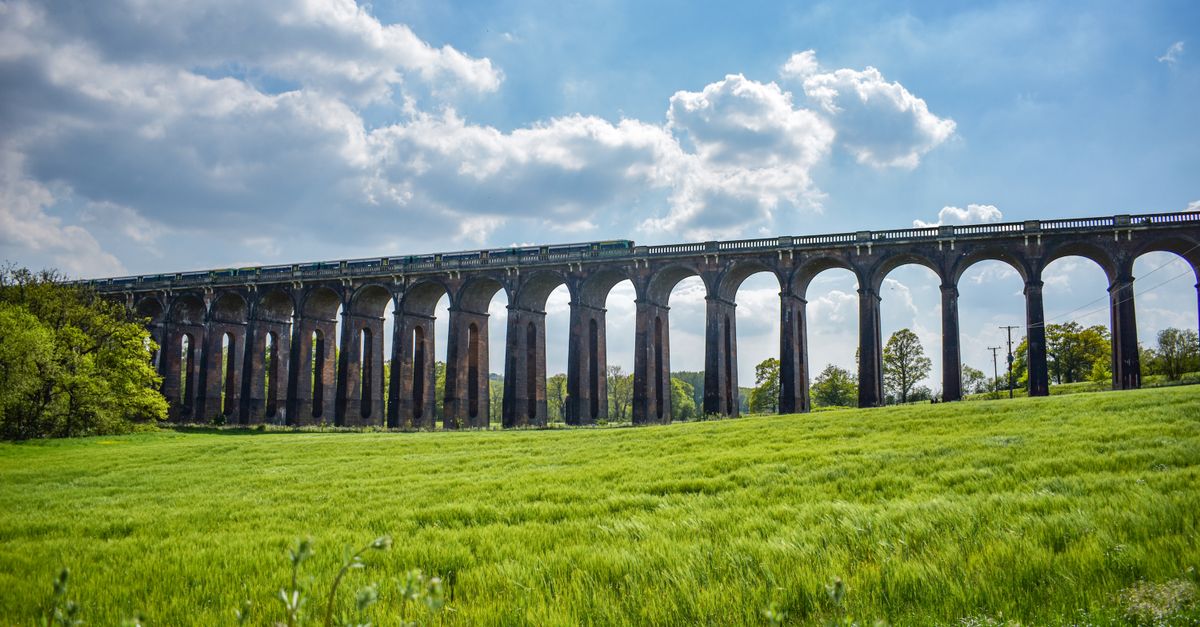 The stunning Ouse Valley Viaduct stretches across a lush green field under a clear blue sky in England.